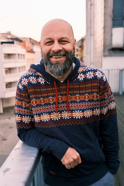 Adam Sobotka, smiling, on a rooftop in a patterned sweater